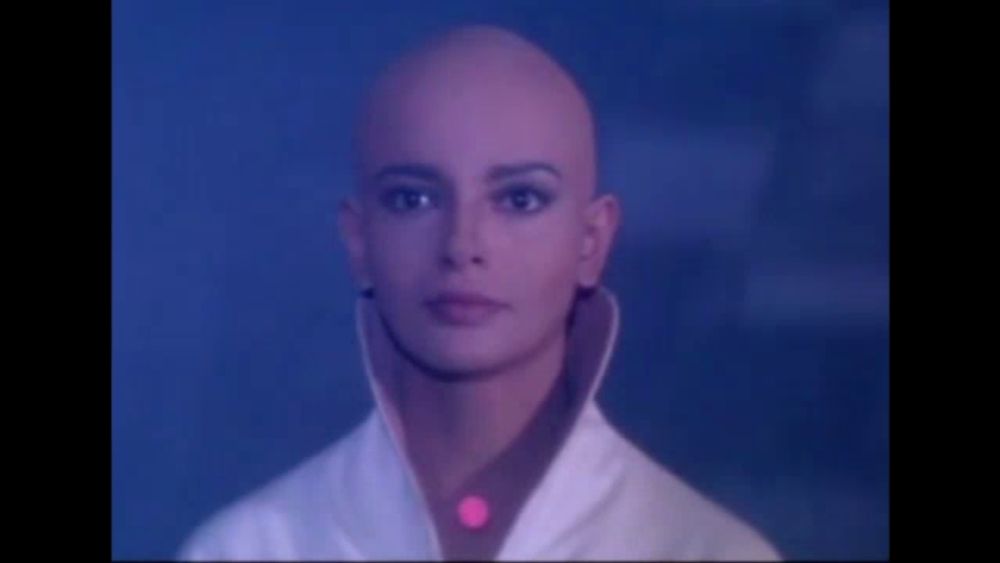 a woman with a shaved head is wearing a white coat and a red shirt .