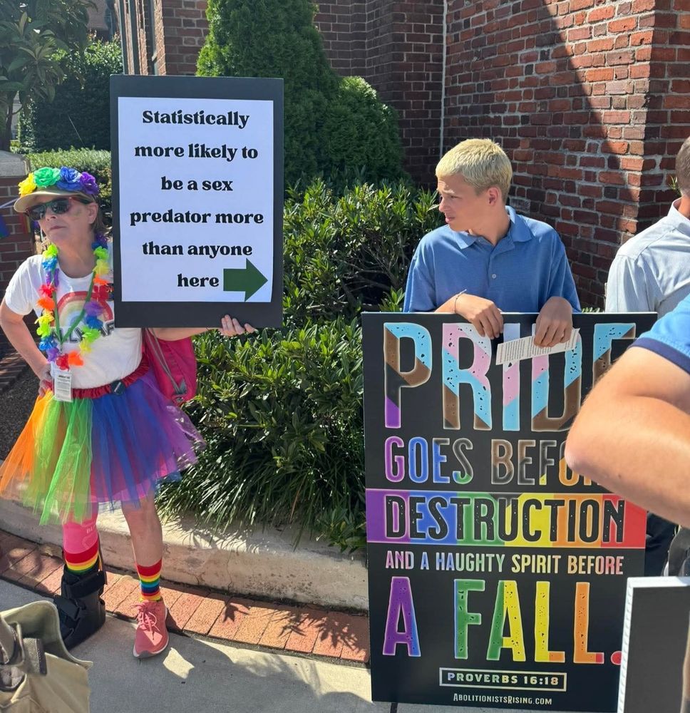 A pride parade attendant holding a sign with "statistically more likely to be a sex predator more than anyone here" pointing at a dude holding a sign with "pride goes before destruction and a naughty spirit before a fall" written on it.