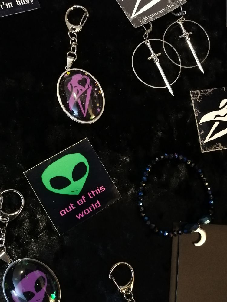 Alien sticker that says "out of this world" sword earrings, sparkly bag charms and a bracelet with a crescent moon