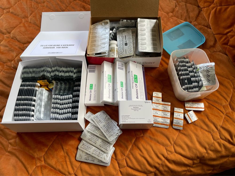 Boxes of medications and some loose, laid out on a burnt orange duvet cover.