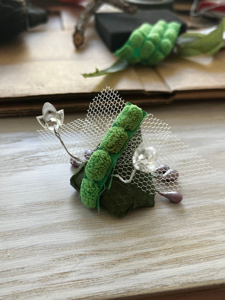 A little green bug made from scrap materials: it has plastic antennae and legs and see through wings 