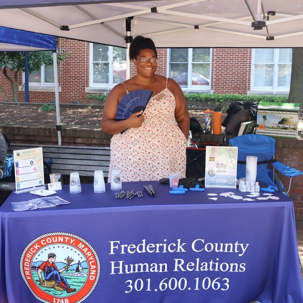 An image of a person standing behind a table, smiling, and holding a fan. 