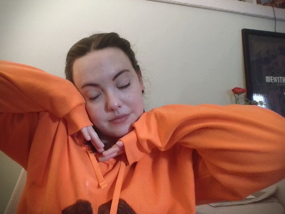 laptop camera selfie of the poster (me, a white woman with brown hair in two braids) wearing an oversized hoodie, with hands posed cutely and demurely under my chin, head tilted and eyes closed, like the "go girl give us nothing" version of a cute selfie