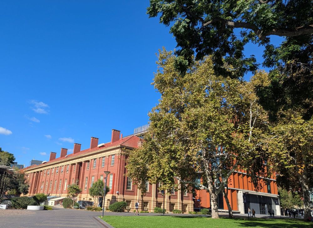 Red brick and sandstone building with a green lawn in foreground and a bright blue sky 