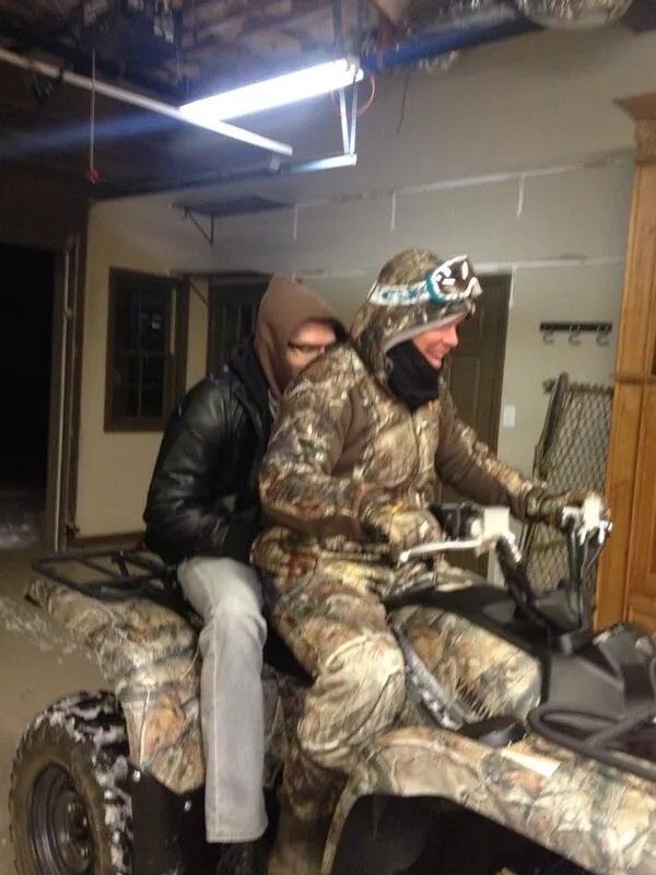 Chipper Jones in all camo on a camo 4 wheeler with Freddy Freeman on the back in grey jeans and a leather jacket over a brown hoodie with the hood pulled up. 