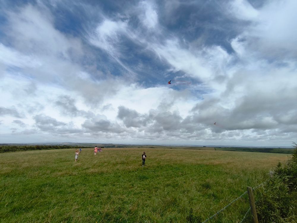 A green hilltop in South Dorset, 4 kite fliers with 2 kites in the air. A sunny summer day with a good mixture of clouds