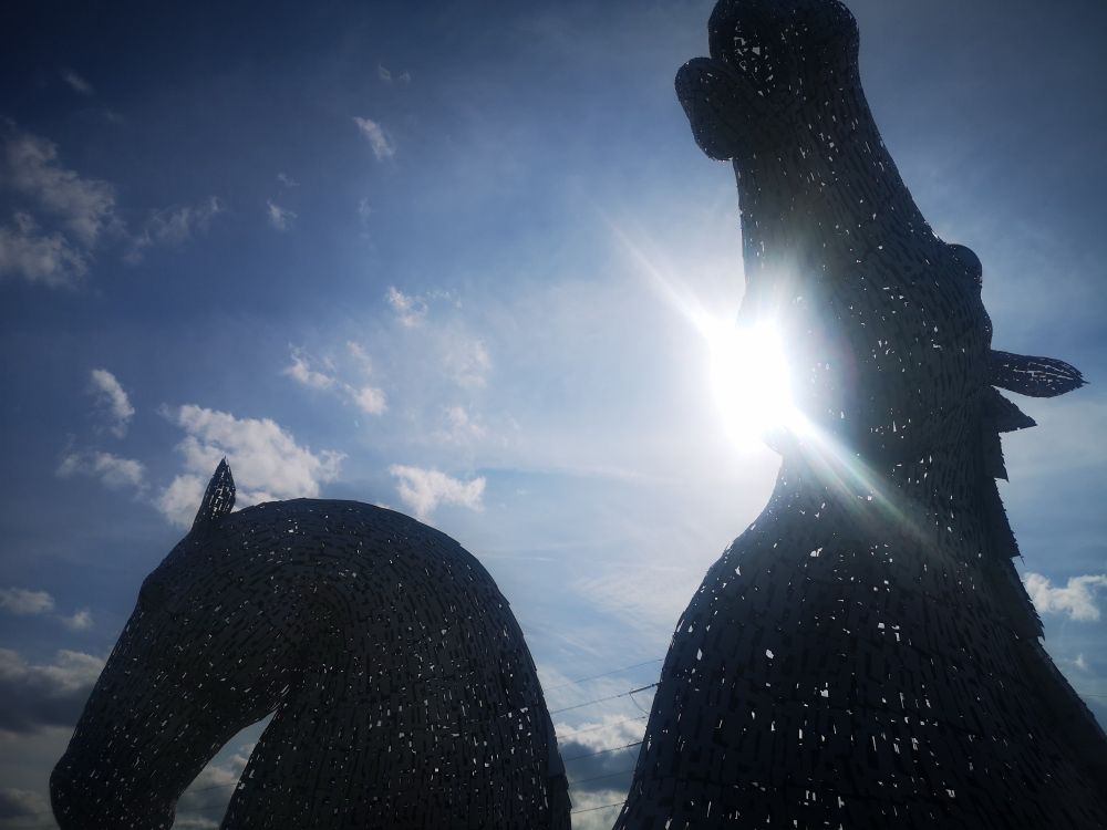 The afternoon sun shines through the Kelpie statues at Falkirk. Two giant horse heads rear into the sky. 