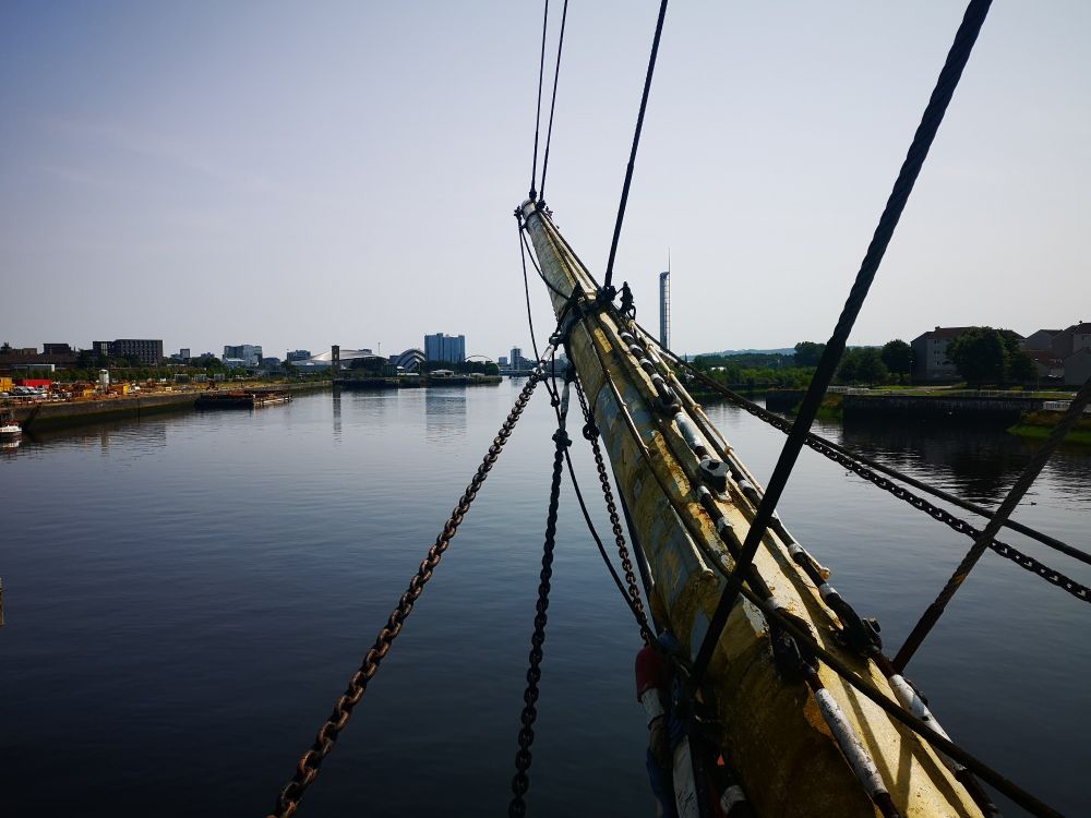 The bow-sprit of The Glen Lee looking inland / upstream on the river Clyde. Taught chains and cables reach the bow-sprit from the top, right and bottom of the photo. The bow-sprit reaches towards the centre top of the photo from the right hand bottom edge of the picture. 