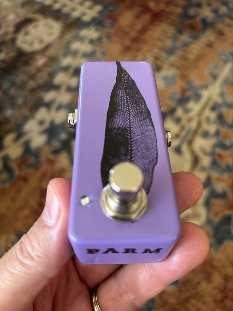 A guitar effect pedal with a single foot switch and no knobs. It is purple and there is a leaf stamped on it in black ink.