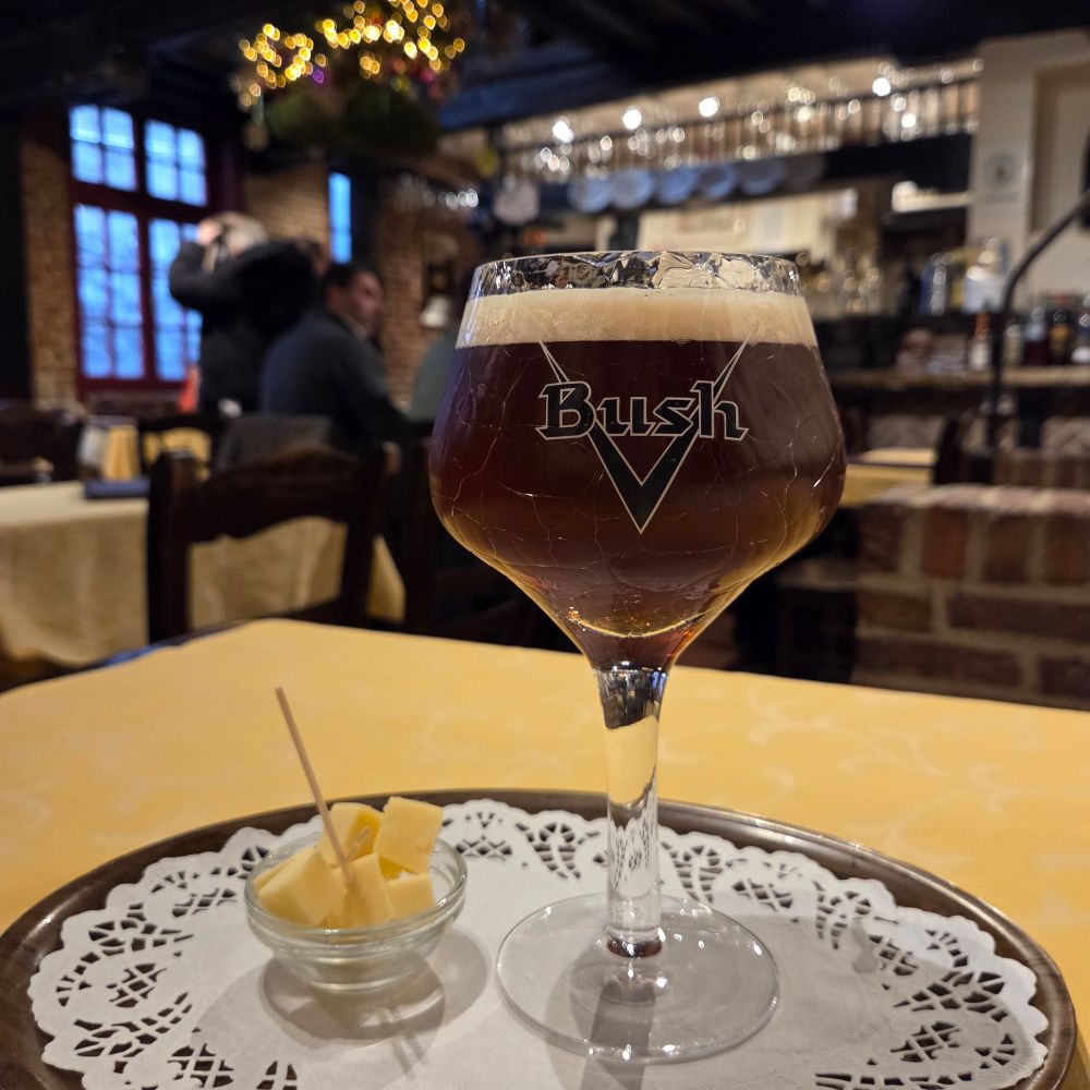 A glass of dark Christmas beer with the traditional cheese portion beside, all served on a wooden tray with white doily. The bar is in the background. 