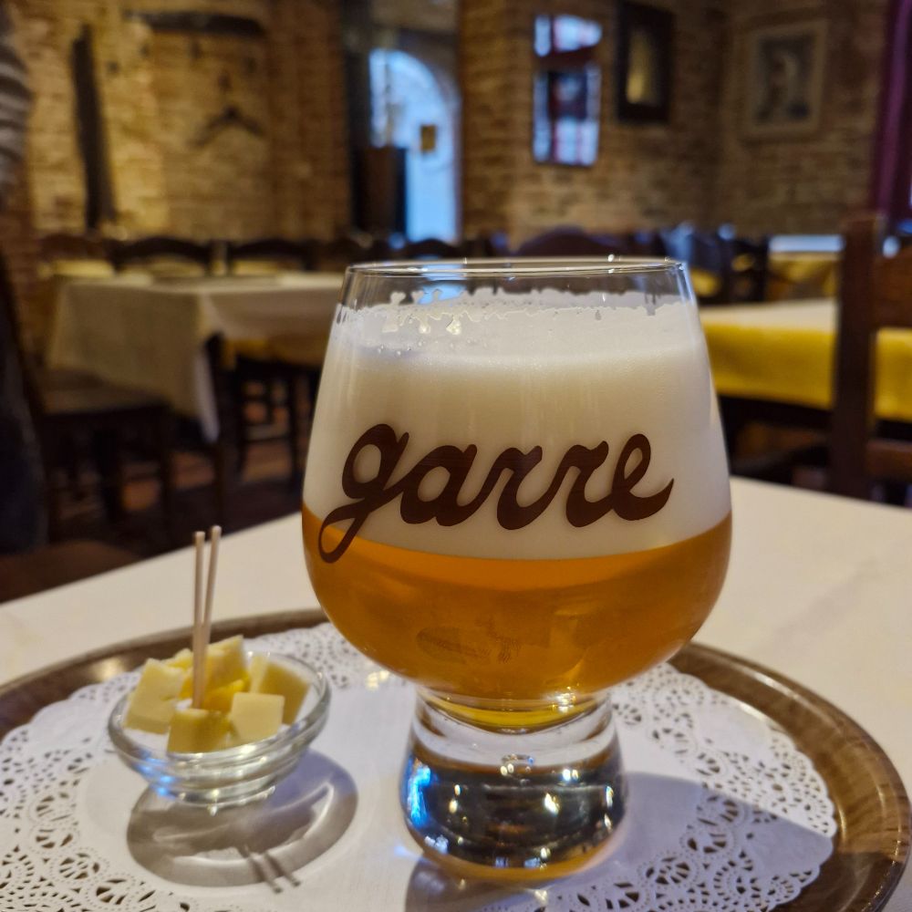 A glass of house tripel at De Garre, Brugge. It's served with the customary small dish of cheese cubes, on a small tray with white doily. 
