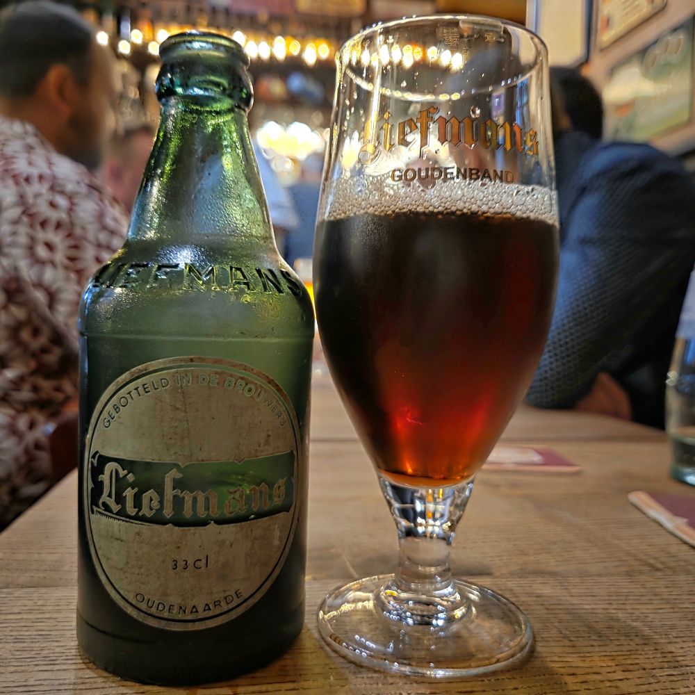A very old bottle of Liefmans Goudenband to the left, with the beer in a glass to the right. 