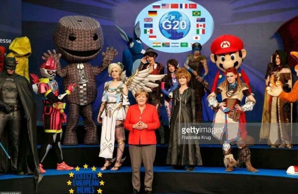 Foto von einer Gruppe Cosplayer (Mario, Sora, Mercy, Batman, Sackboy, etc.) mit Angela Merkel im Vordergrund