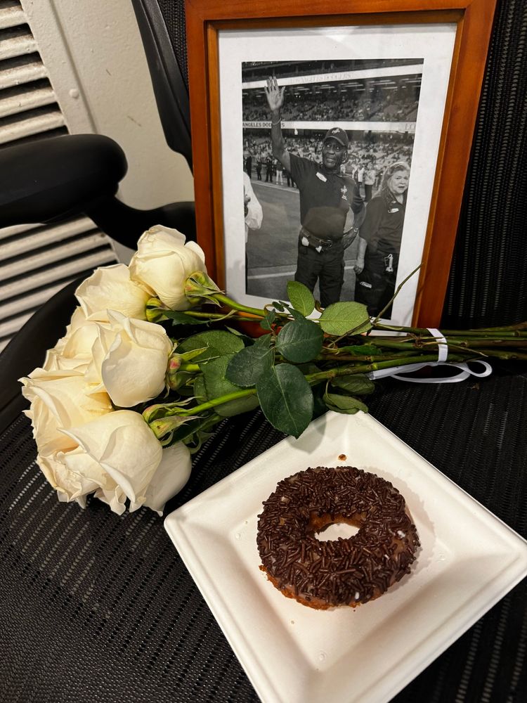 a picture of longtime Dodger Stadium employee James Mims, who passed away this weekend. Flowers and a donut laid in front of the photo. Mims worked security at Dodger Stadium for a half century.