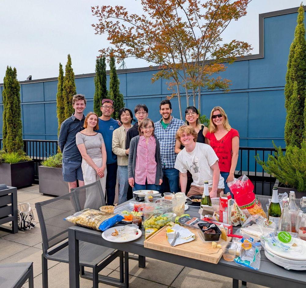 Group of people posed for a photo. There's a table full of food in front of them. 