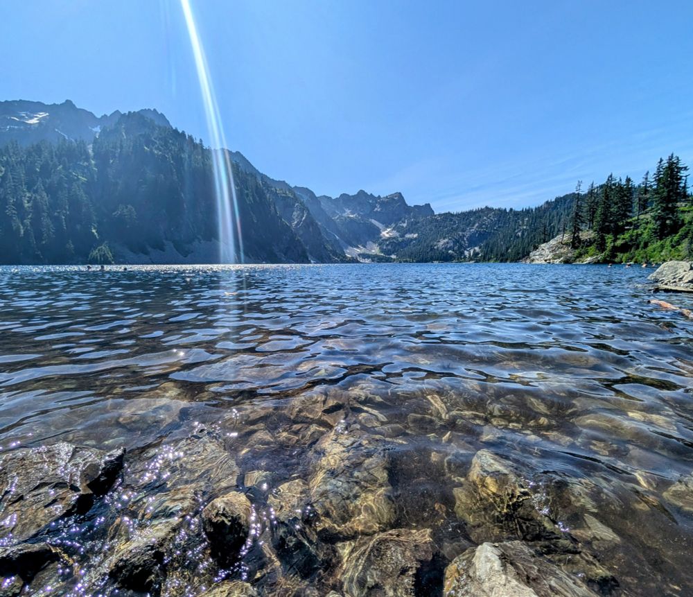 Crystal clear glacial lake view very close to the water. There's a big sunbeam streaming through the picture. 