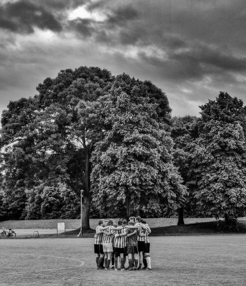 A monochrome image of a huddled amateur football team, under leaden German skies. The background is of big trees. The image gives no indication whatsoever that this team is about to lose 1-0 to a collection of German men in their fifties and sixties.