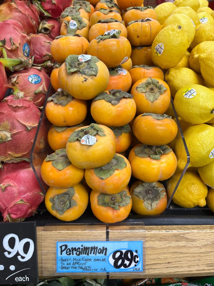 Yellowish Persimmons on a grocery display, the price tag says 89c/each.