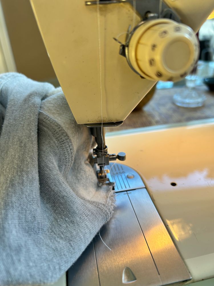 Gray sweatshirt being mended on a sewing machine 