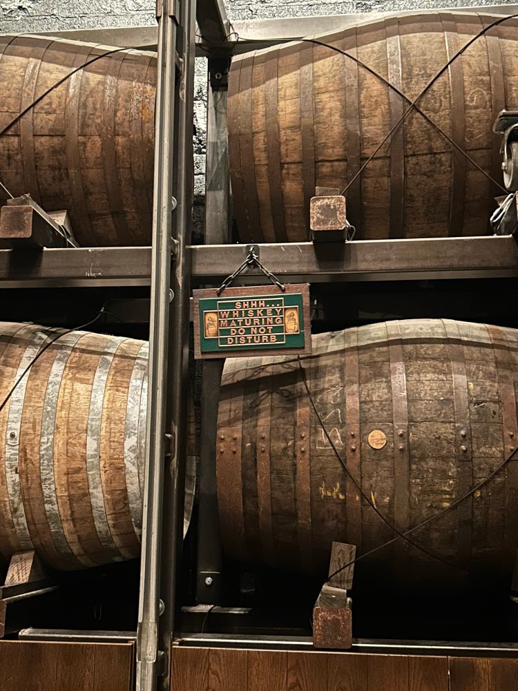 some bourbon casks at the jameson distillery with a sign that says “shhh…. whiskey maturing do not disturb”