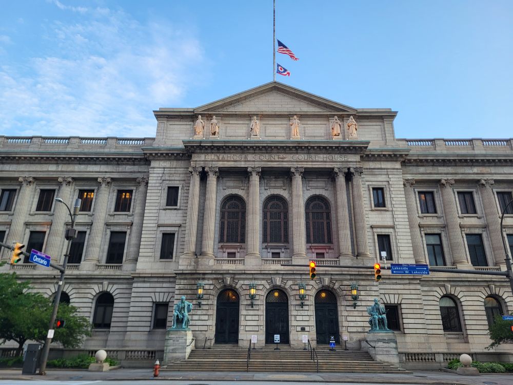 Flags fly at half mast atop a neo-Classical building that is the Cuyahoga County Courthouse.