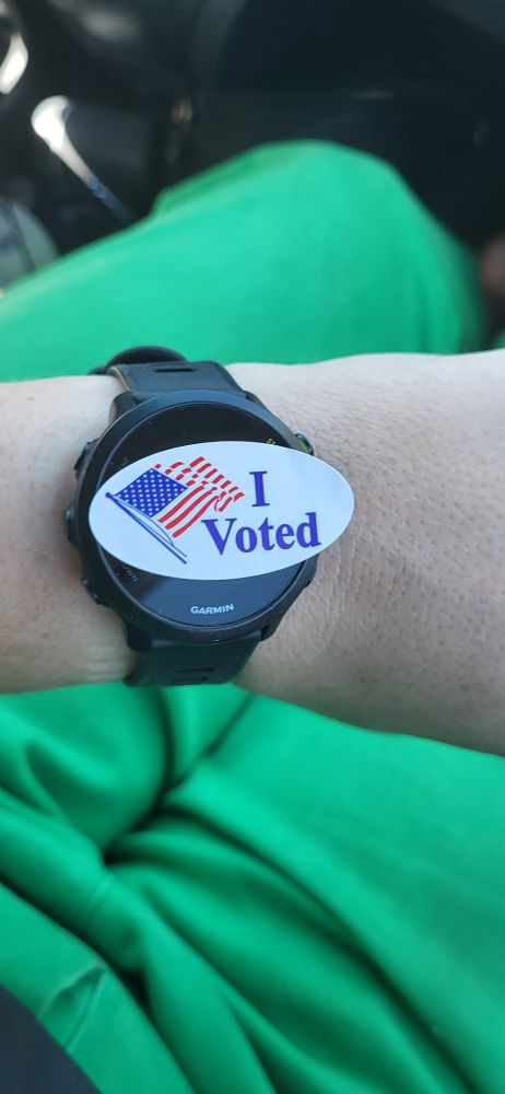 An i voted sticker on my wristwatch with green pants on the background 