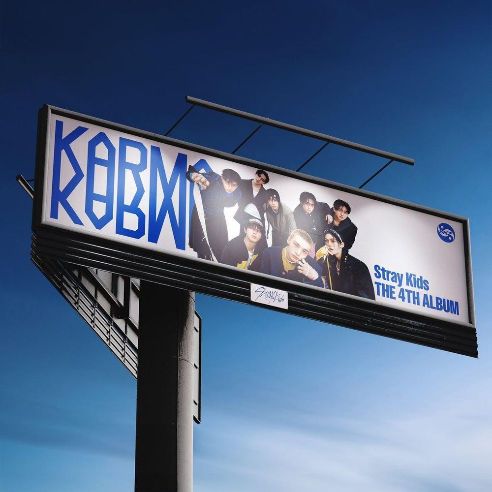 the new digital cover for Karma! it's a picture of a billboard with an ot8 skz photo on it and KARMA written in big blue letters!