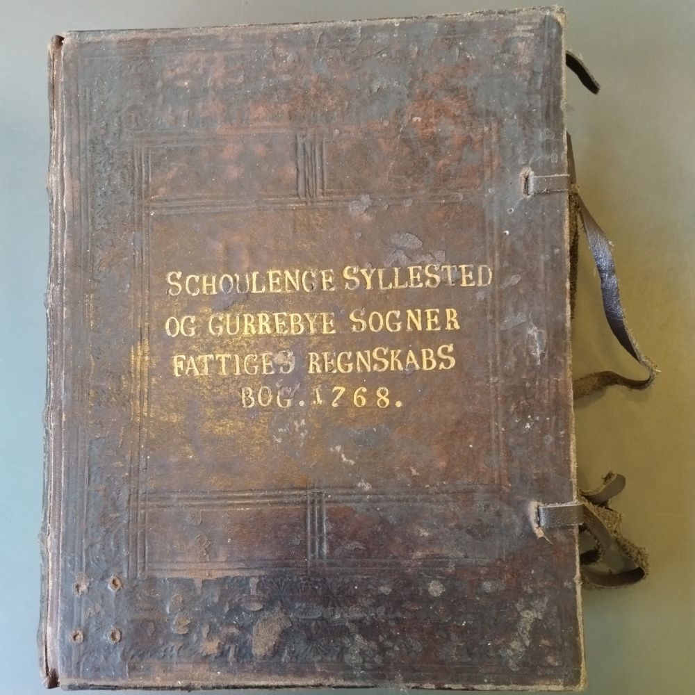 Danish government book from 1768. Bound in brown leather with a golden printed title on the cover. Leather laces on the side to bind the front and back of the cover together.