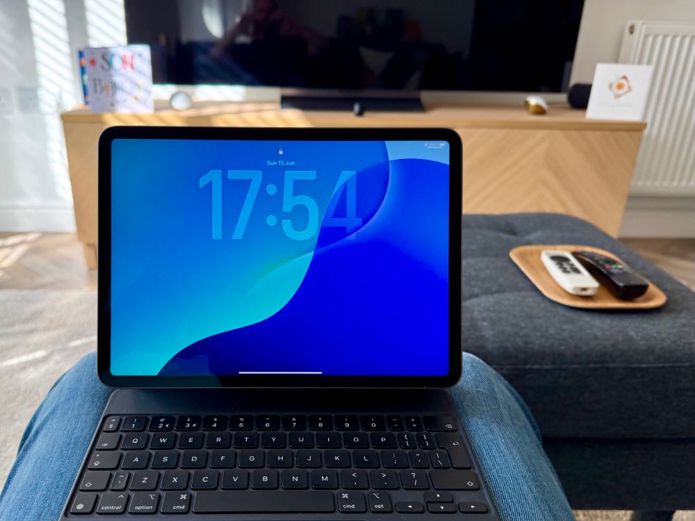 my iPad on my lap in my lounge, running iPadOS26 showing the Home Screen with the time in big numbers