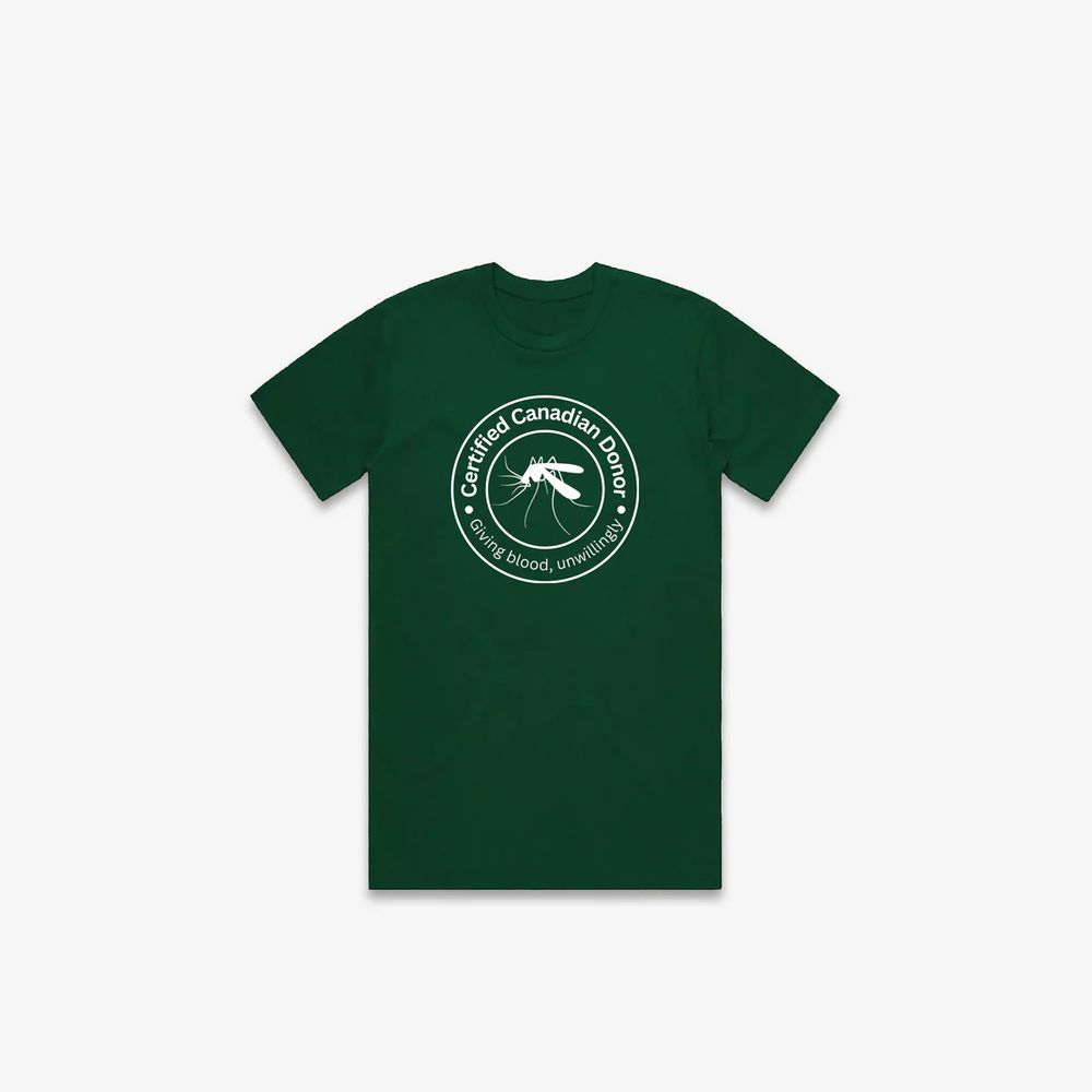 A forest green T-shirt with 2 white circles on the chest. A white outline of a mosquito is contained in the inner circle. A description in white lettering is inside the outer circle ‘Certified Canadian Donor . Giving blood, unwillingly .’