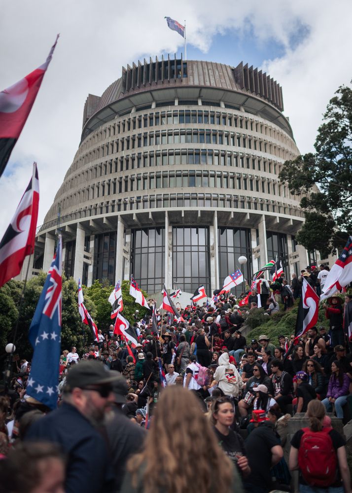 The Beehive, the centre of government in New Zealand, surrounded by protestors carrying many flags, predominantly Tino Rangatiratanga