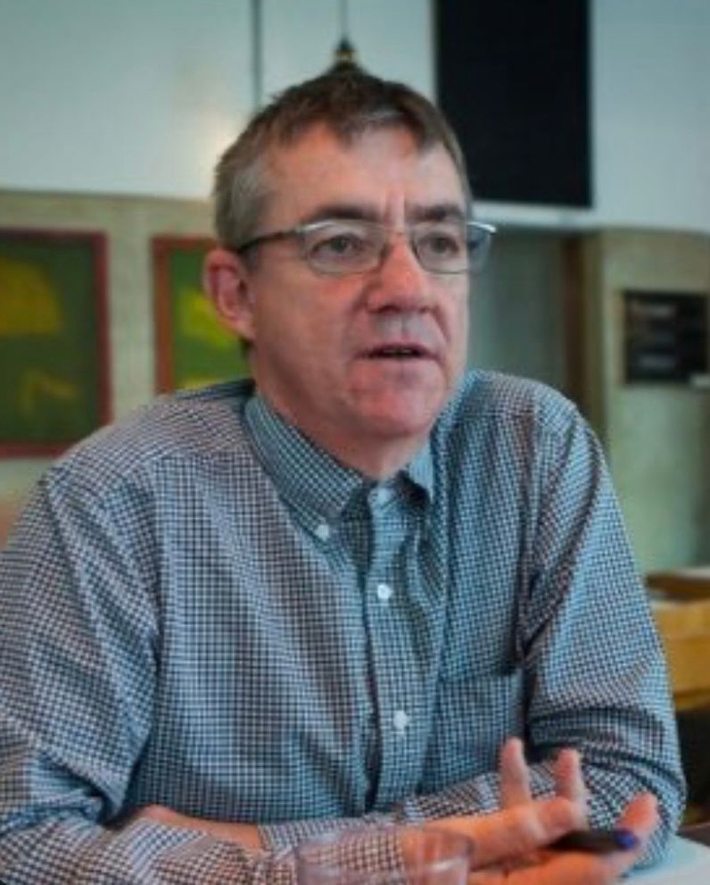 John McTernan’s Twitter profile picture: he is in a blue checked shirt and talking to someone we can’t see