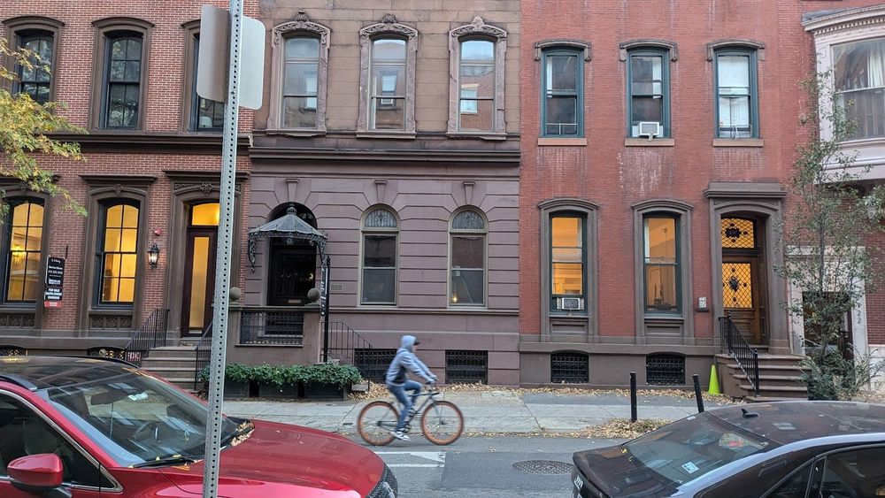 A person in a grey hoodie rides in the Spruce St bike lane, with rowhomes in the background and parked cars in the foreground