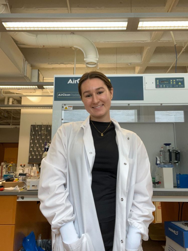Headshot of Amanda Ellis standing in the lab, wearing a lab coat. Photo provided by Amanda Ellis. 