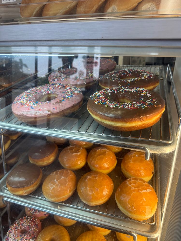 A donut case, on the top shelf are some unusually large donuts (about the size of an adult head!), pink and chocolate with sprinkles. 