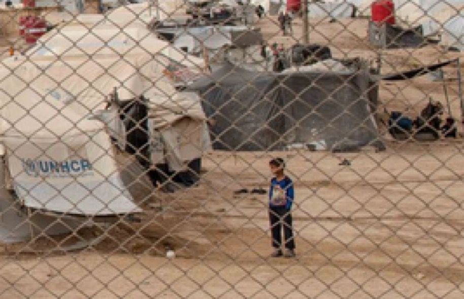 Un enfant derrière les grilles d’un camp.