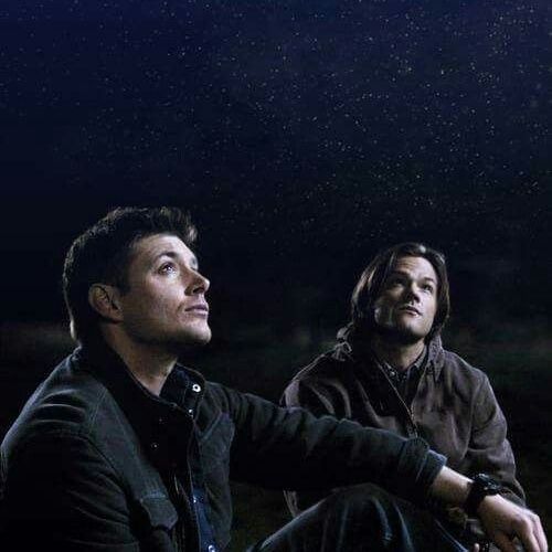 Sam Winchester (Jared Padalecki) and Dean Winchester (Jensen Ackles) sit together outdoors at night, gazing up at a sky filled with stars in supernatural 