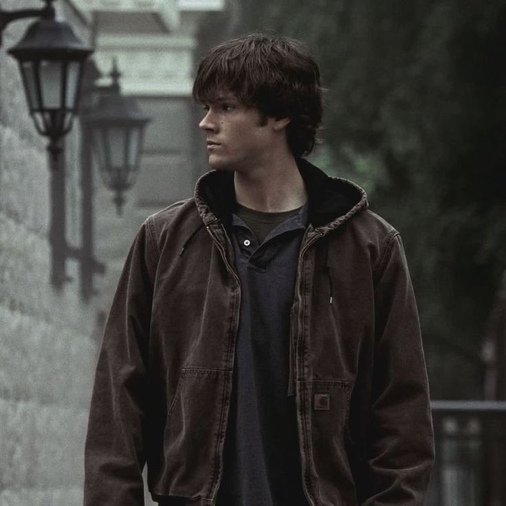 Sam Winchester (Jared Padalecki) stands in a dimly lit alley, wearing a brown jacket hoodie, with vintage street lamps in supernatural 