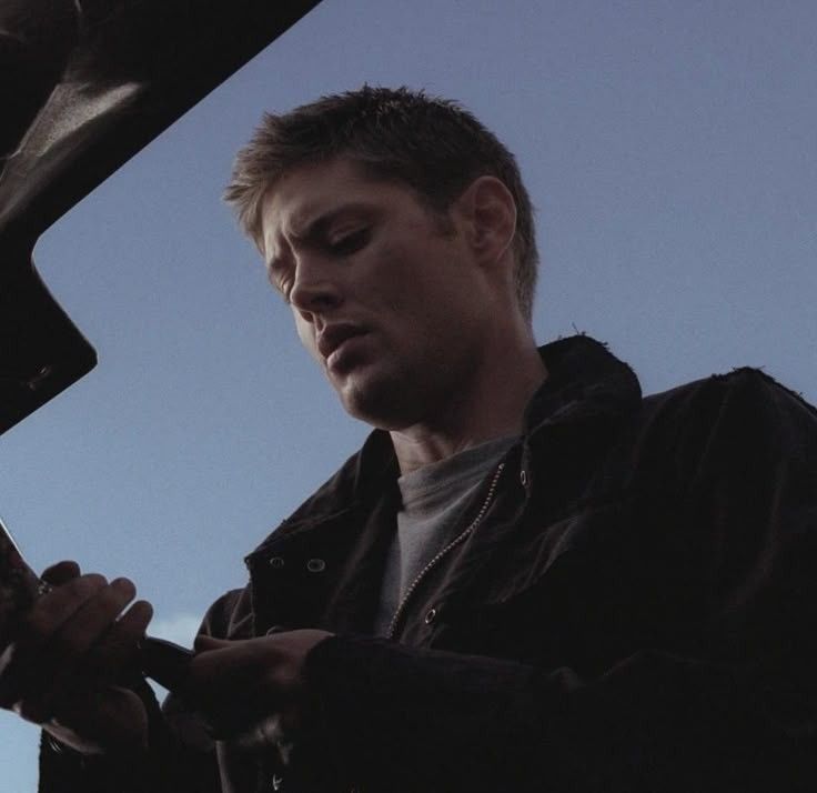 Dean Winchester (Jensen Ackles) stands at the boot of baby, against a backdrop of a clear evening sky in supernatural 