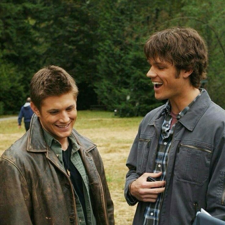 Sam Winchester (Jared Padalecki) Dean Winchester (Jensen Ackles) stand together in a grassy field, surrounded by trees, wearing casual clothing and sharing a conversation in supernatural 