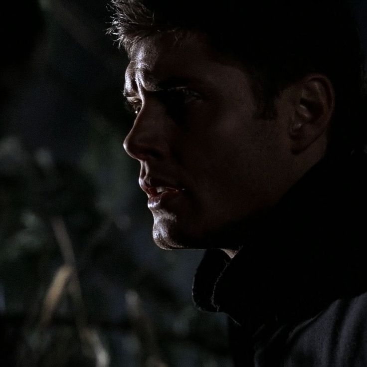 A close-up of a dark silhouette of Dean Winchester (Jensen Ackles) against a blurred, shadows-filled backdrop, highlighting an ear and neck in low light in supernatural 