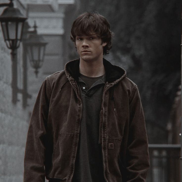 Sam Winchester (Jared Padalecki) stands in a dimly lit alley, wearing a brown jacket hoodie, with vintage street lamps in supernatural 