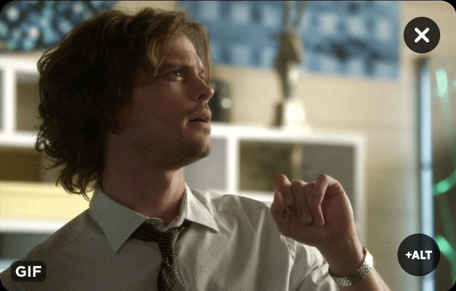 Spencer Reid (Matthew gray gubler) with curly hair gestures confidently, wearing a light shirt and tie, in a modern, brightly lit room in criminal minds