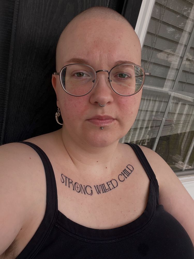 Harper is a white person with a shaved head, glasses, and a “strong willed child” chest tattoo. 