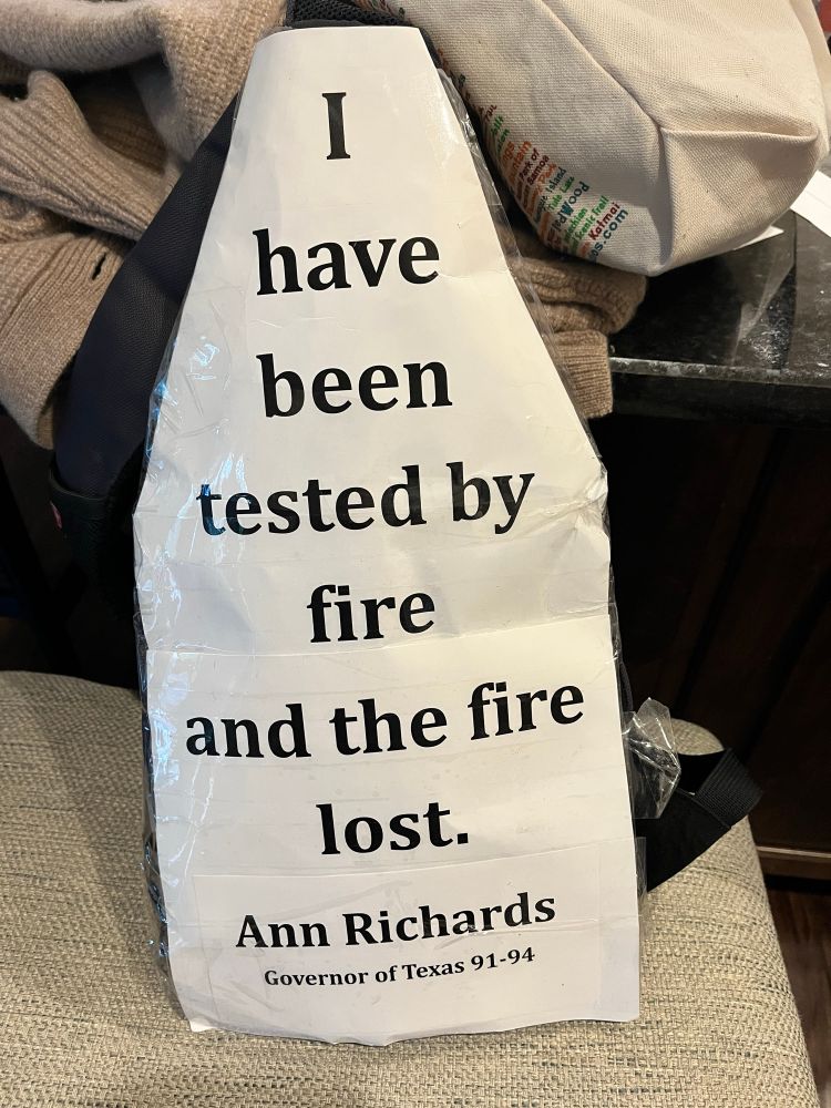 Small backpack with a white sign taped to it reading: I have been tested by fire and the fire lost. - Ann Richards Governor of Texas 91-94