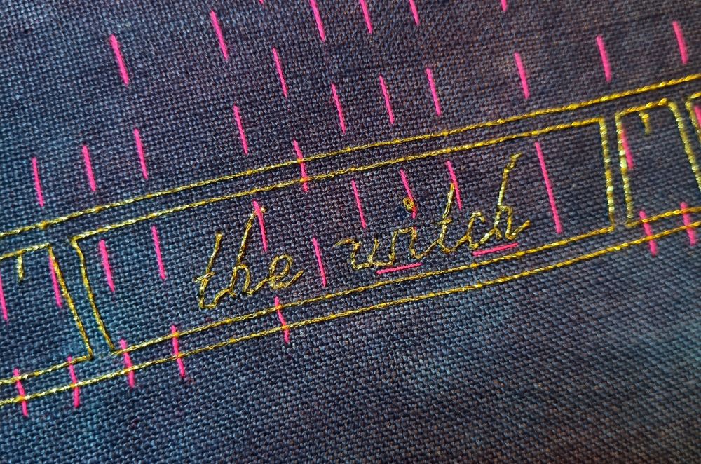 Metallic gold backstitch reading "the witch" 