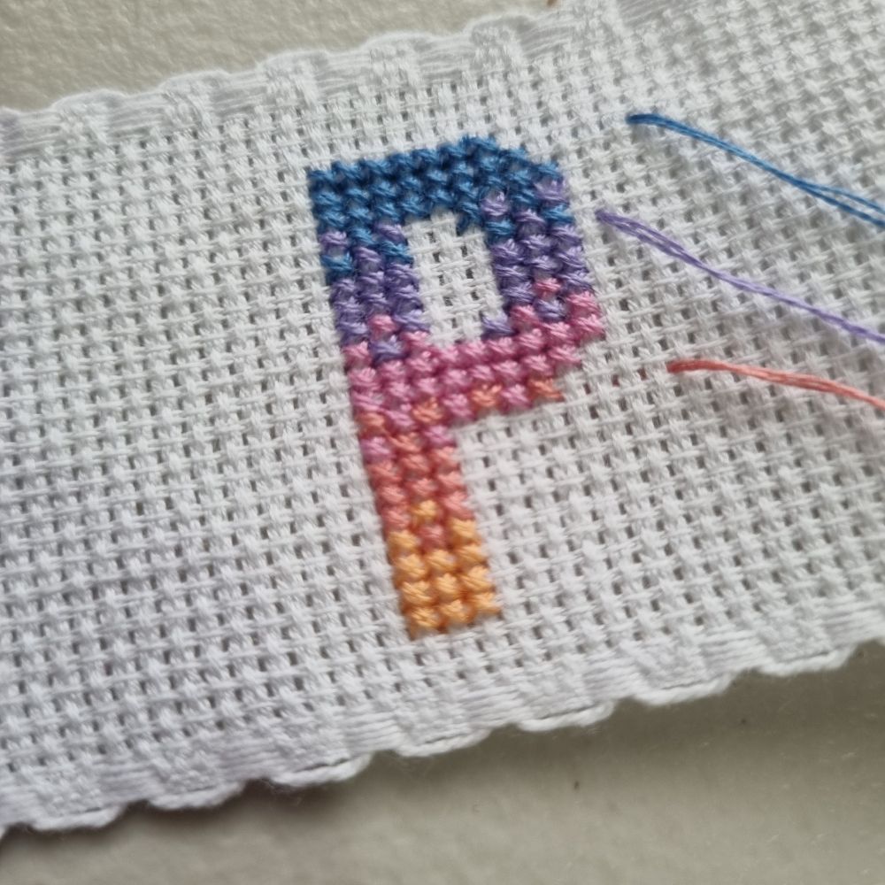 Cross stitch of the letter "P" in a blue to orange sunset gradient.