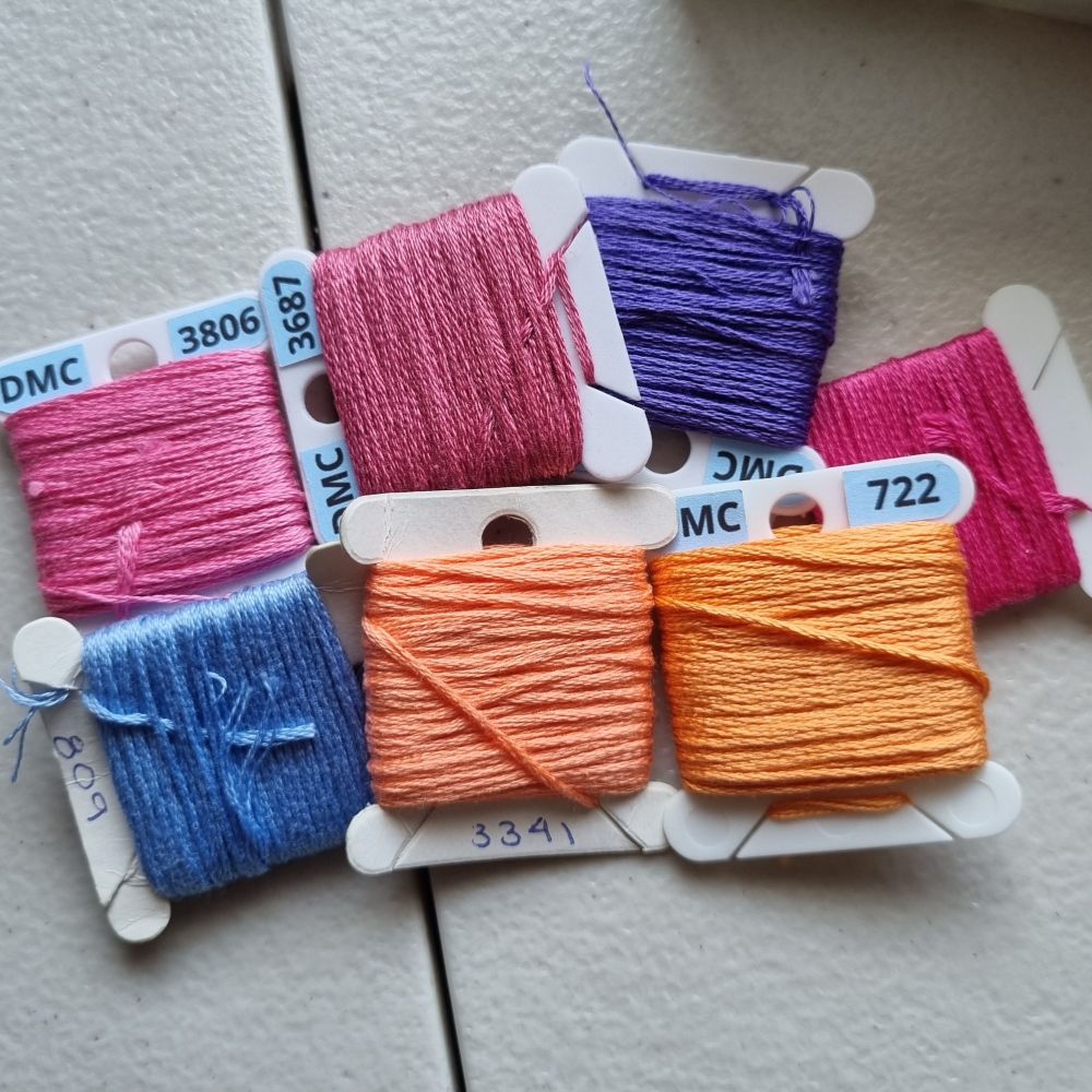 Pile of embroidery thread bobbins in oranges, pinks, purple, and blue.