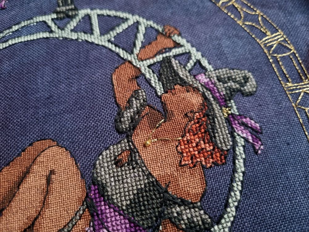 Close up of cross stitched witch showing off her black and purple hat, curly red hair, and golden necklace