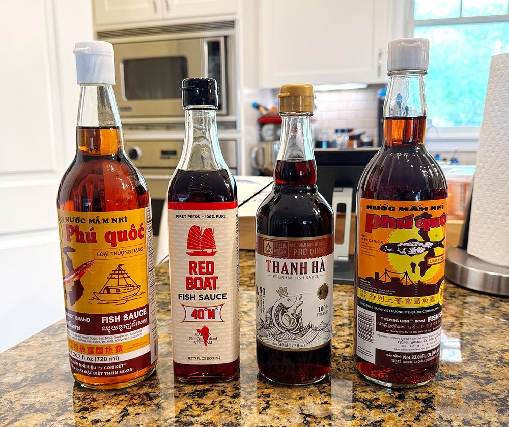 Four bottles of fish sauce standing on a kitchen counter — Double Parrot, Red Boat, Thanh Ha and Flying Lion.